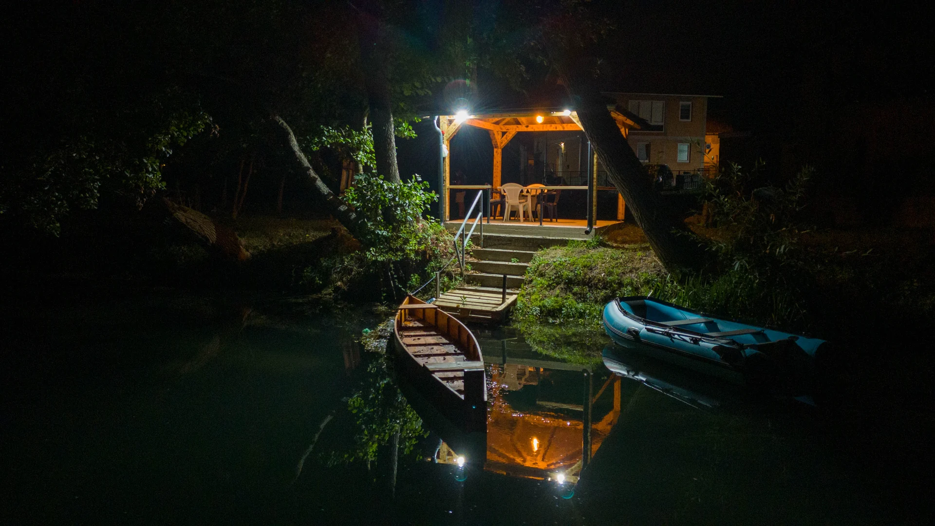 Beleuchteter Pavillon und Boote spiegeln sich nachts in der Pliva